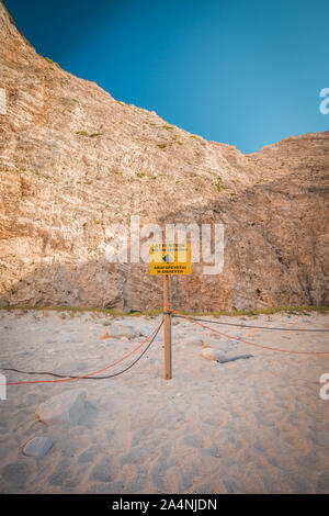 No Trespassing sign on a pole with rope near cliff, warning falling rocks, Greece Zakynthos beach Navagio near shipwreck. Rear shot from behind. Stock Photo