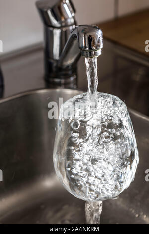 Water flows from a tap into a glass. Symbol: water consumption, waste of water. Stock Photo