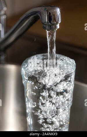 Water flows from a tap into a glass. Symbol: water consumption, waste of water. Stock Photo