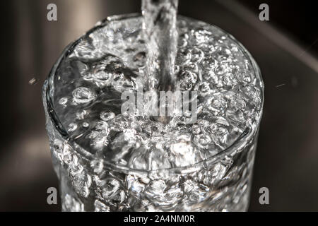 Water flows from a tap into a glass. Symbol: water consumption, waste of water. Stock Photo