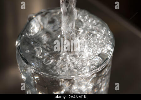 Water flows from a tap into a glass. Symbol: water consumption, waste of water. Stock Photo