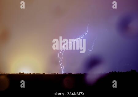 Double lightning strike hits the earth with rainfall during stormy weather. Rain drops are on the lens. Stock Photo