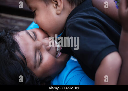 A little brother gives his big sister a kiss on her cheek while she laughs out loud in joy. Stock Photo