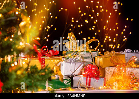 Stack of packed gift boxes under Christmas tree against particles lights. Lots of Christmas gifts under the tree. Selective focus on green box gift! Stock Photo