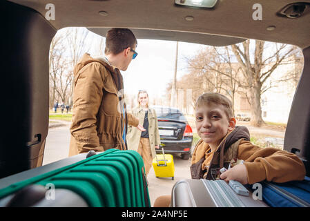 family with kid putting bag in car trunk Stock Photo
