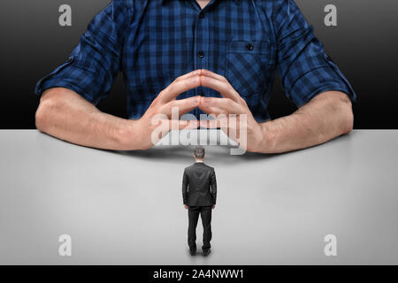 Businessman stands in front of big man sitting with his fingers clasped Stock Photo