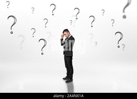 Thoughtful businessman looking upwards surrounded by question marks on white background Stock Photo