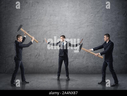 Businessman separating two fighting businessmen with hammers Stock Photo
