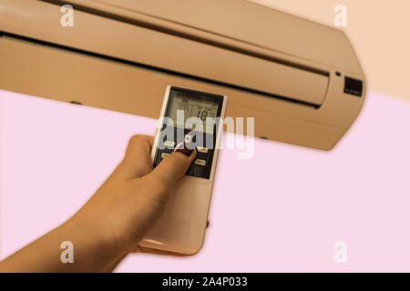 Woman hand using air conditioner remote controller. Air temperature control indoors. Stock Photo