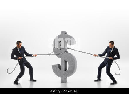 Two businessmen pulling big concrete 3d dollar sign with ropes in opposite directions isolated on white background Stock Photo