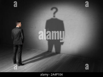 Businessman looking at question mark instead of head his shadow. Stock Photo