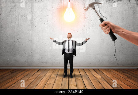Hand holding a hammer going to break glowing bulb over businessman's head. Stock Photo