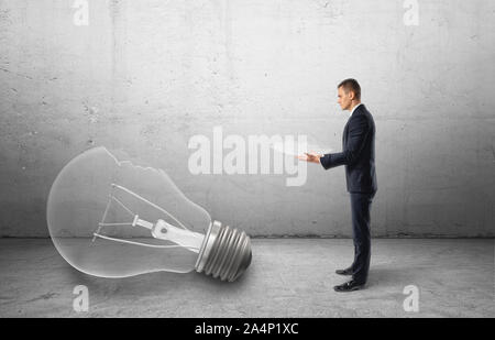 Big broken bulb fallen to the floor and businessman holding a piece of it Stock Photo