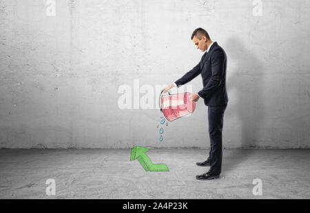 Businessman holding red bucket with water pouring out of it on green arrow pointing up Stock Photo