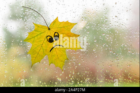 Autumn maple leaf on glass, view from the window. Copy space. Raindrops texture. The concept of bad mood. Stock Photo