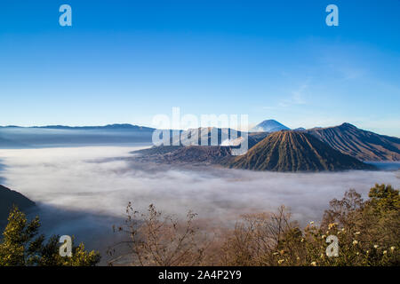 Mount Bromo volcano, island of East Java, Indonesia. Clouds cover the valley floor; Luhur Poten Temple at the foot of the cone. Stock Photo