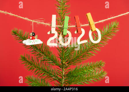 Christmas composition with wooden figures 2020. Figures hang on clothespins on a twine with a Christmas tree branch on a red background Stock Photo