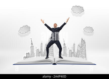 Happy businessman standing with his arms up on big opened book Stock Photo