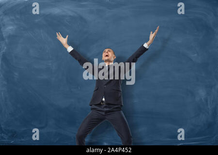 Businessman standing with splayed arms and shouting on the blue blackboard background. Stock Photo