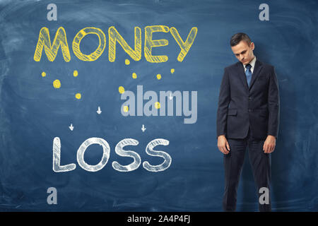 Sad businessman standing near the words 'money loss' written on dark blue wall Stock Photo