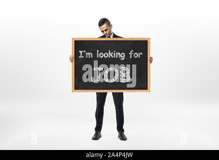 Businessman standing and holding blackboard with words 'I'm looking for job' written on it Stock Photo