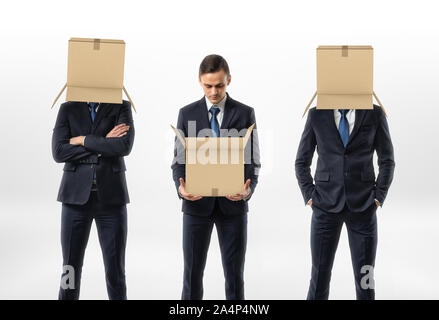 Businessman holding an open cardboard box, the other two are wearing the boxes on their heads. Stock Photo
