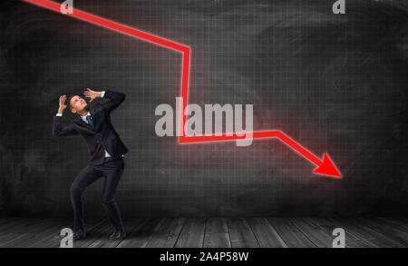 Small frightened businessman under huge red kinked arrow pointing down Stock Photo