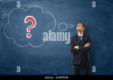 Businessman on blue blackboard background where thoughts bubbles with a red question mark are drawn in chalk. Stock Photo