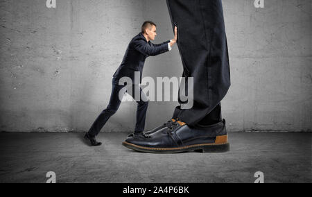 Little businessman is pushing a big boss's huge feet on gray background Stock Photo