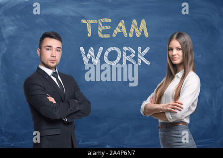 Businessman and businesswoman on blue chalkboard background with words 'Team Work' Stock Photo