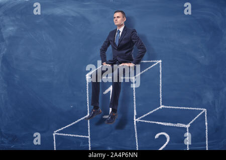 Businessman is sitting on the first place of a podium on blue blackboard background Stock Photo