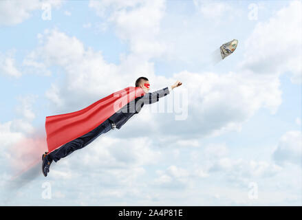 A businessman in a superhero cape flying in the sky trying to catch a 100 USD banknote. Stock Photo
