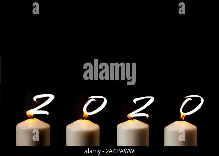 Marry Christmas and happy New Year. 2020 is written with candle flames on black background. Concept of greeting card. Top view, flat lay, copy space. Stock Photo