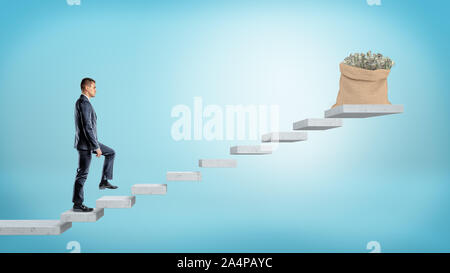 A businessman walking concrete steps made of flying grey slabs to reach a money bag full of dollar bills. Stock Photo