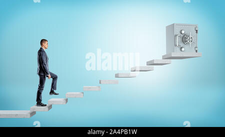 A businessman on blue background going upstairs to a large metal safe box on concrete blocks. Stock Photo