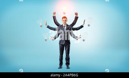 A businessman with many hands surrounded by light bulbs with one of them lighted up. Stock Photo