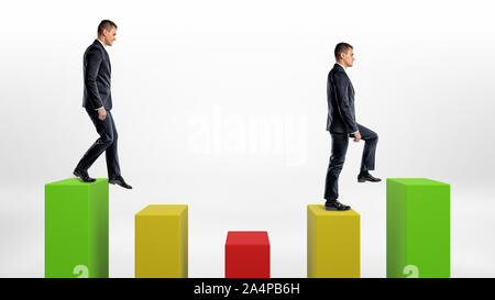 Two businessmen on white background stepping up and down green, yellow and green statistic columns. Stock Photo