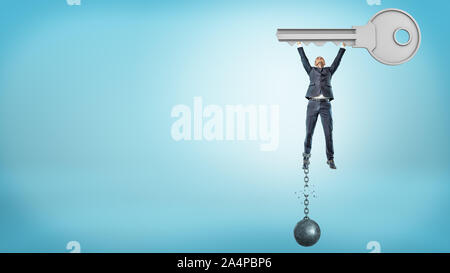 A small businessman holds up a huge metal key while getting free from a broken ball and chain. Stock Photo