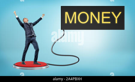 A victorious businessman stands on a large red pushbutton that's connected to a monitor with a word MONEY. Stock Photo