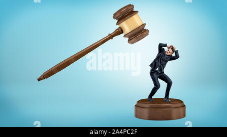 A small businessman tries to avoid a giant gavel strike while standing on a sound block. Stock Photo