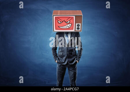 A self-assured businessman holds his hands in pockets and wears an old TV with an angry smiley face on his head. Stock Photo