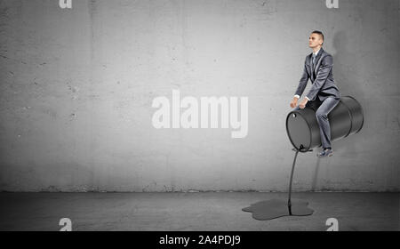 A small businessman sits on a black barrel leaking oil like on a horse. Stock Photo