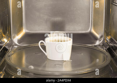 Tea cup inside the microwave. Warming the tea on the microwave. Stock Photo