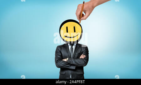 A businessman with crossed hands stands in front view while a giant hand draws a smiley face instead of his head. Stock Photo