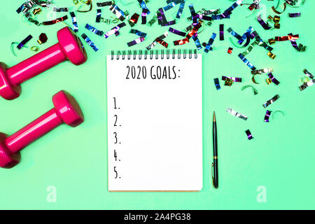 Goals list for New Year Holiday. Christmas sport set with dumbbells, notebook with pen and colorful confetti on on pastel mint green blue background. Flat lay, top view, copy space. Stock Photo