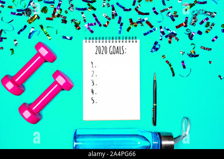 Goals list for New Year Holiday. Christmas sport set with dumbbells, notebook with pen, bottle of waterwater and colorful confetti on mint green blue color background. Flat lay, top view, copy space. Stock Photo