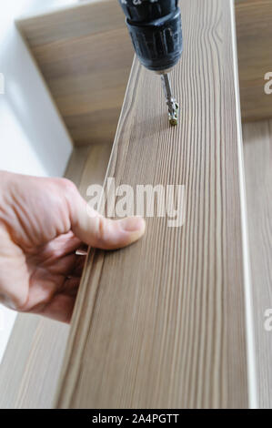 A man is installing a hook for clothes. He is using a screwdriver to fix the bracket hook. Stock Photo