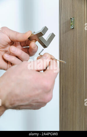 A man is installing a hook for clothes. He is using a hex key to fix the bracket of the hook. Stock Photo