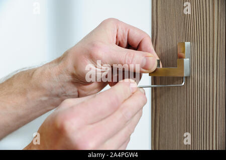 A man is installing a hook for clothes. He is using a hex key to fix the bracket of the hook. Stock Photo