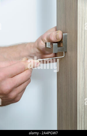 A man is installing a hook for clothes. He is using a hex key to fix the bracket of the hook. Stock Photo